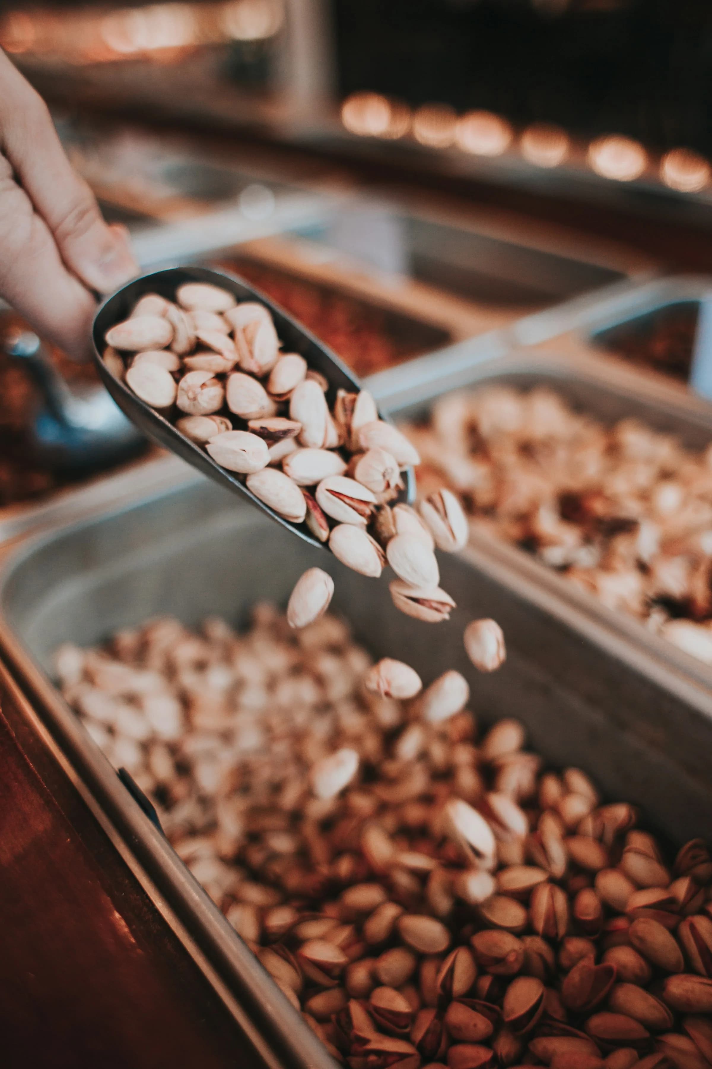 A scoop of fresh pistachios being lifted from a bulk bin